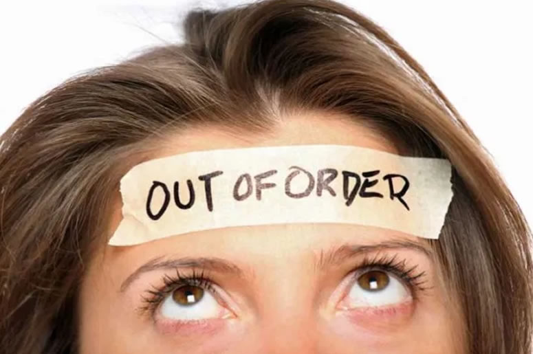 A close up of a lady's eyes and forehead. She's looking up at a sticker on her head with 'Out of Order' written on it.