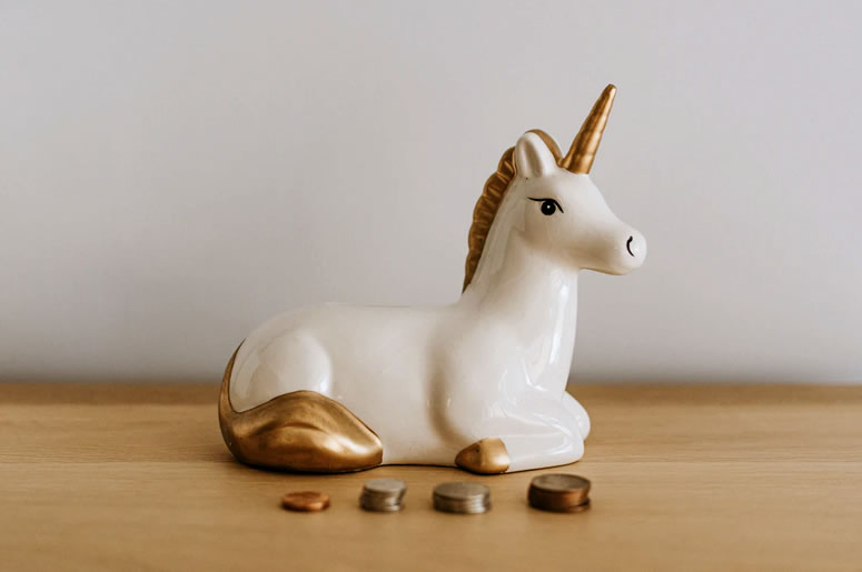 White and gold ceramic money box in the shape of a unicorn, with four small piles of coins stacked up in front: Protecting Your Super