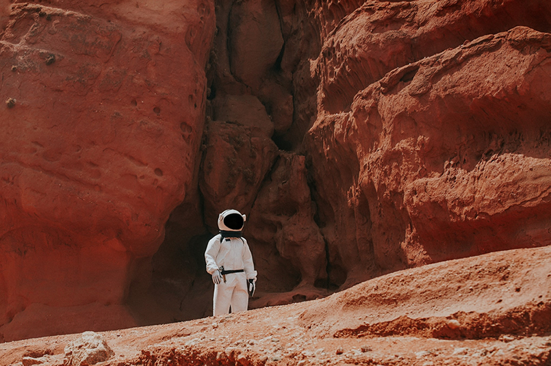 Are Men & Women Worlds Apart with Financial Thinking?: A lonely man in a white astronaut space suit, in a red, rocky landscape resembling the surface of Mars.