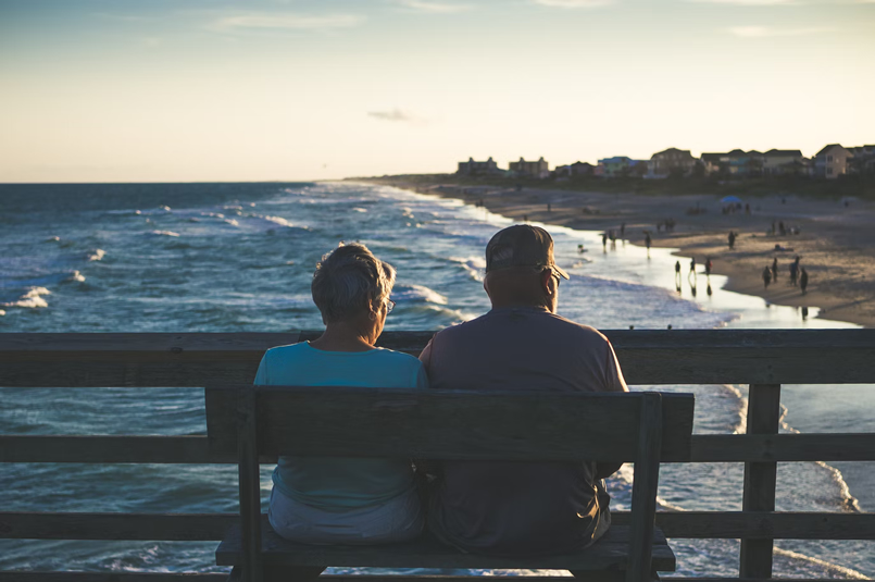 Retirement Income Covenant: A retired couple sitting on a pier bench, admiring the evening view of the beach.