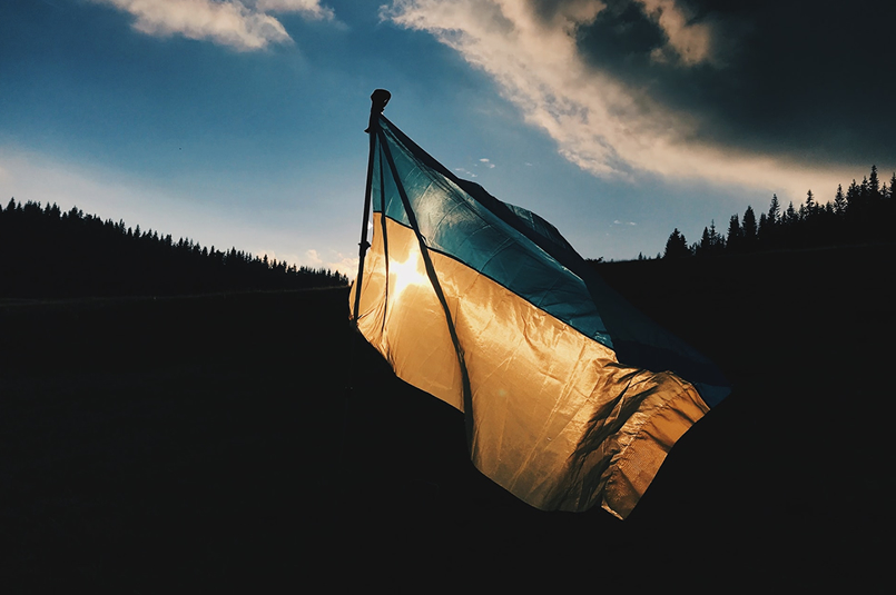 Geopolitics & Investment Markets: A Ukrainian flag with the setting sun shining through from behind.